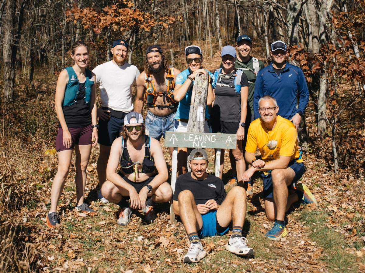 A group posing on the trail with a sign that reads 'Leaving NC.'